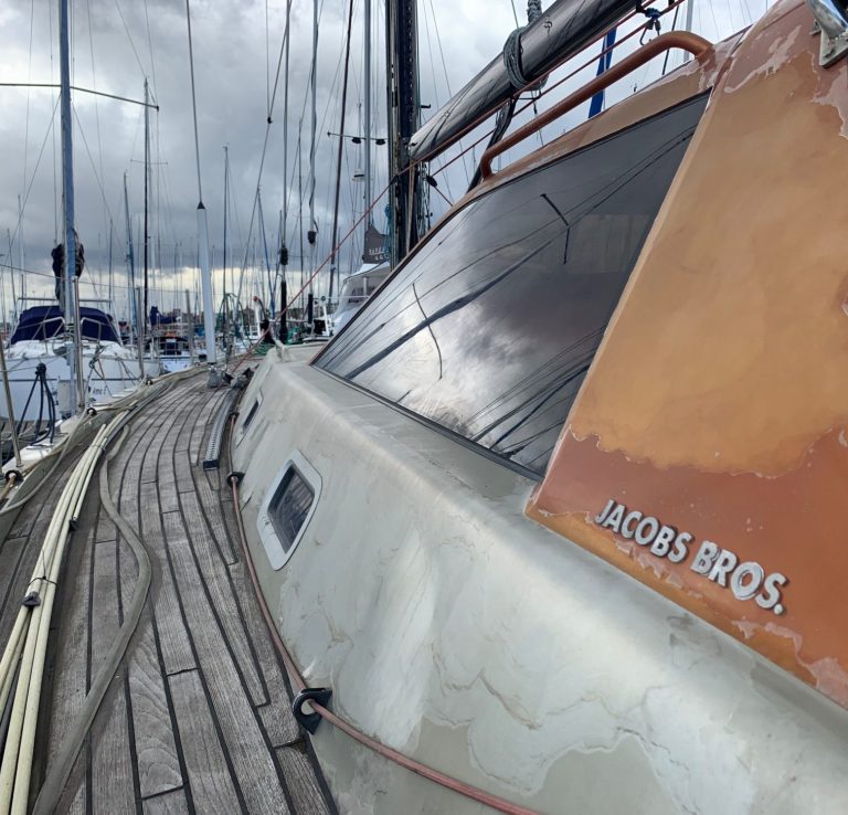 Unwind Sailing Yacht during viewing in Cape Town Sailboat docked, with a prominent "Jacobs Bros." sign and cloudy skies overhead.